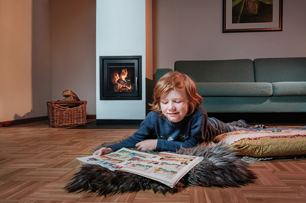 Kind liest auf dem Boden liegen Comic, im Hintergrund der angezündete Kamin