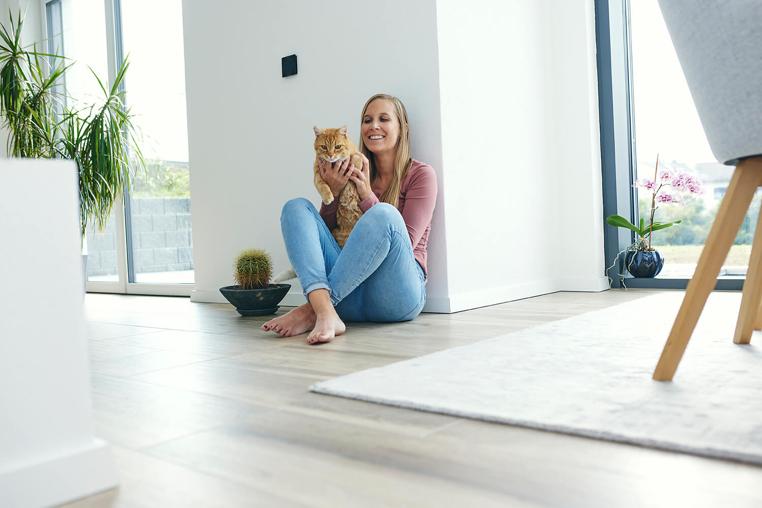 Eine Frau sitzt mit einer Katze auf dem Schoß im Wohnzimmer auf dem Fußboden. 