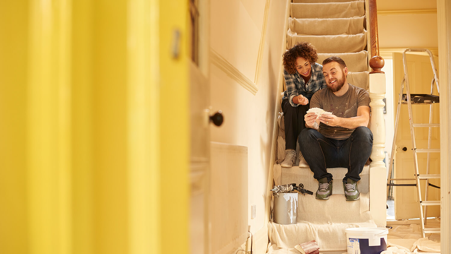 Ein junges Paar sitzt auf der Treppe in einem Haus, das gerade renoviert wird.
