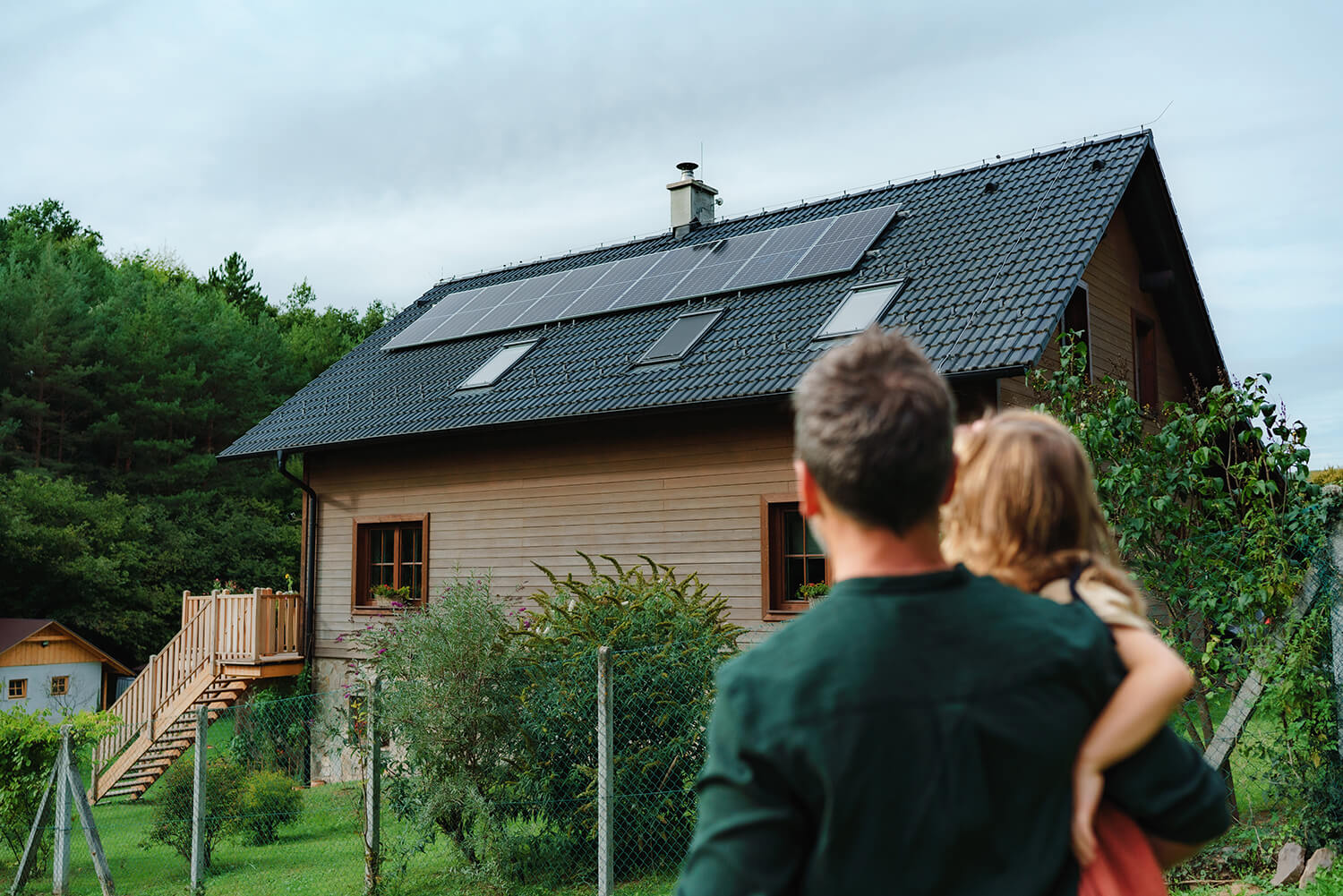 Ein Mann mit einem Mädchen auf dem Arm steht vor einem Haus mit einer Solaranlage auf dem Dach. 