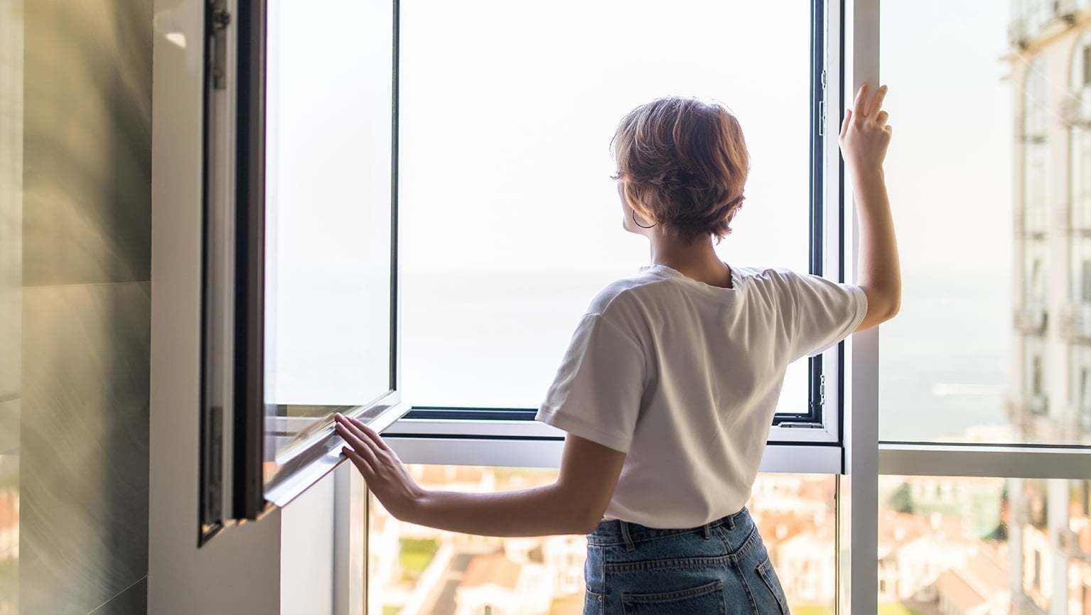 Eine Frau steht an einem geöffneten Fenster und schaut raus.